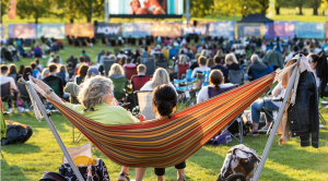 Two women sitting on a hammock in the foreground with the rest of the audience in the background alongside an outdoor cinema screen